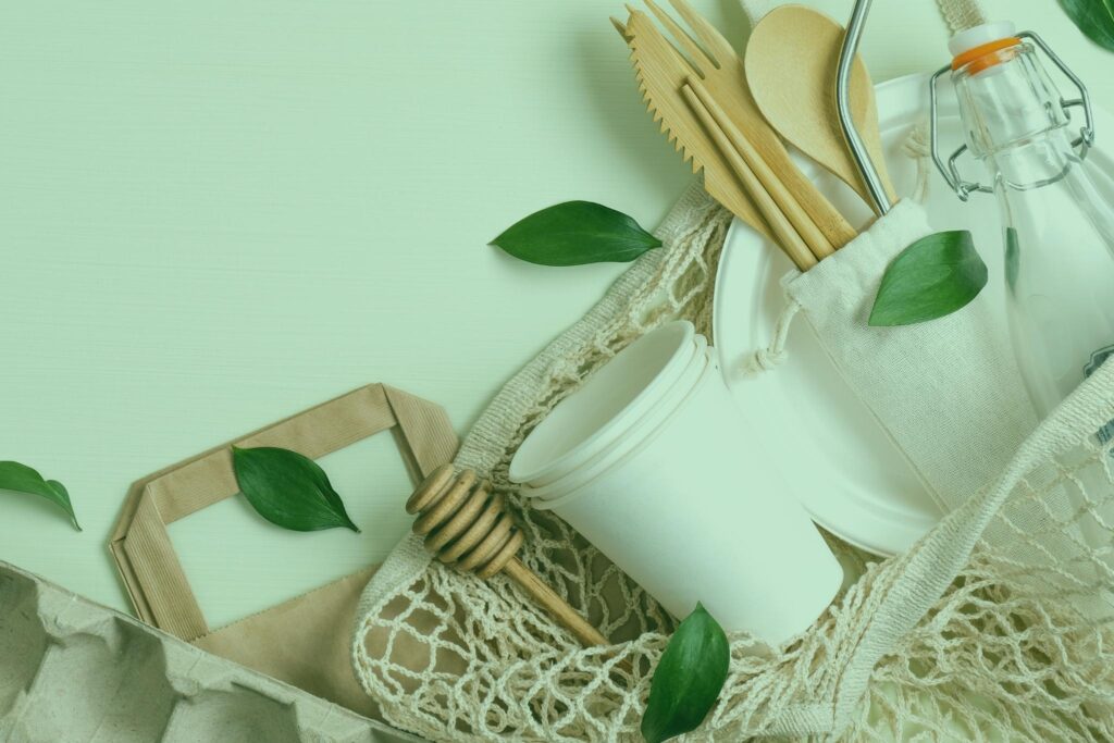 Fundo branco com copos de papel e utensílios reciclados de cozinha.