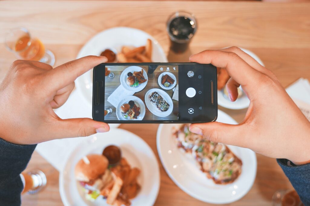 Mãos tirando foto de comida em mesa banco de imagens