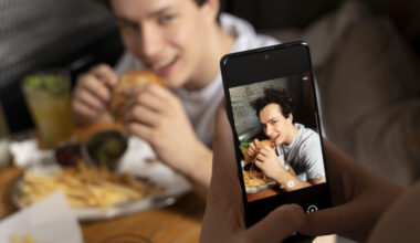 Celular tirando foto de homem mordendo um hamburguer.