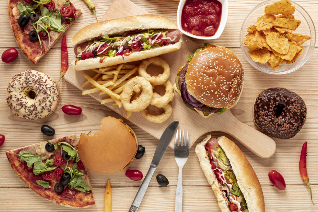 Mesa com várioss tipos de comida food service posicionadas, como pizza, hambúrguer e nachos.