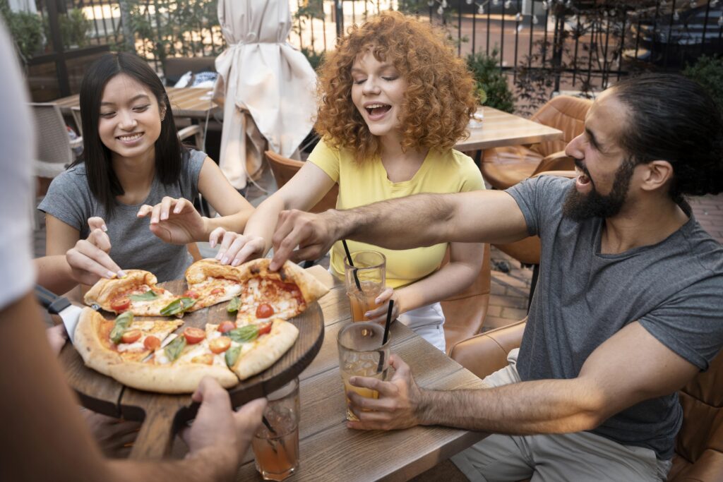 Grupo de pessoas em pizzaria se servindo, felizes e conversando.