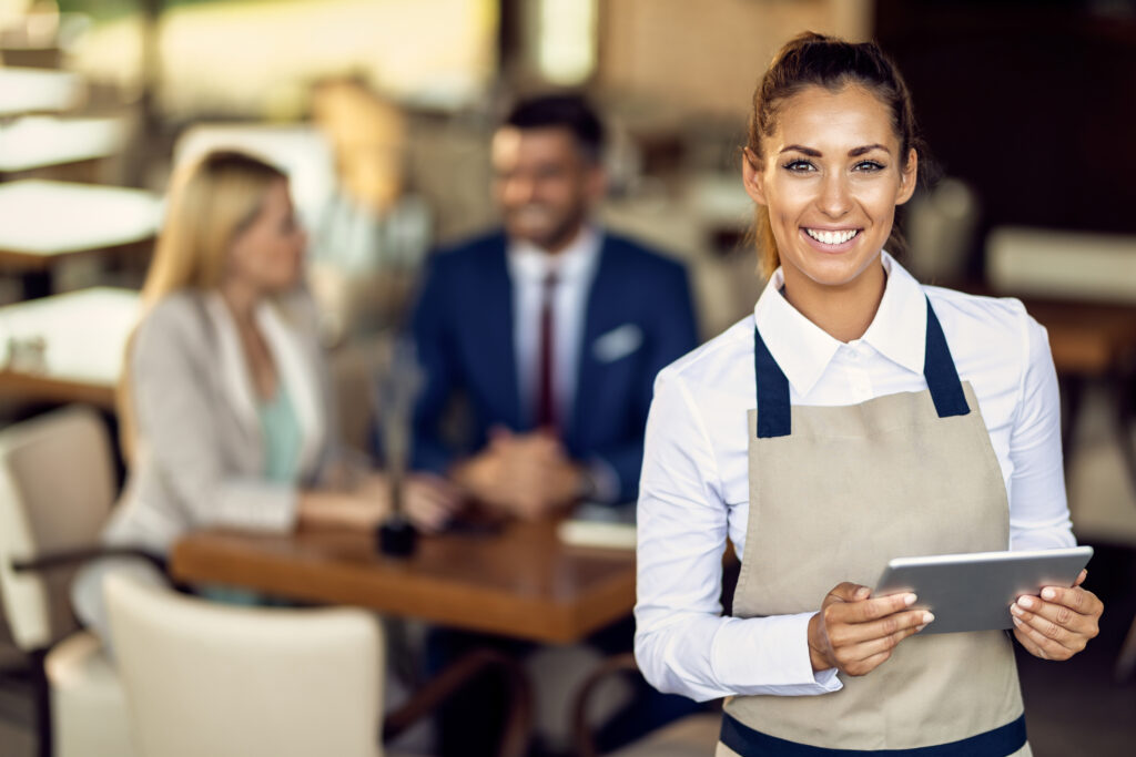 Atendente de restaurante bar sorrindo para câmera com tablet na mão