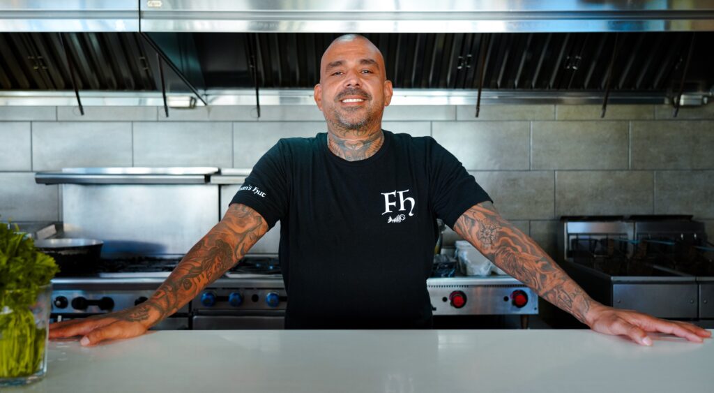 Dono de bar em cozinha sorrindo para câmera