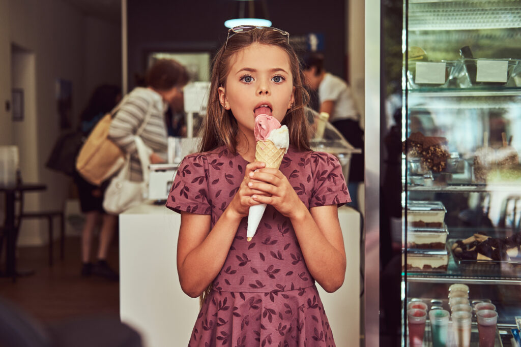 Criança tomando casquinha de sorvete em frente a loja de açaí.
