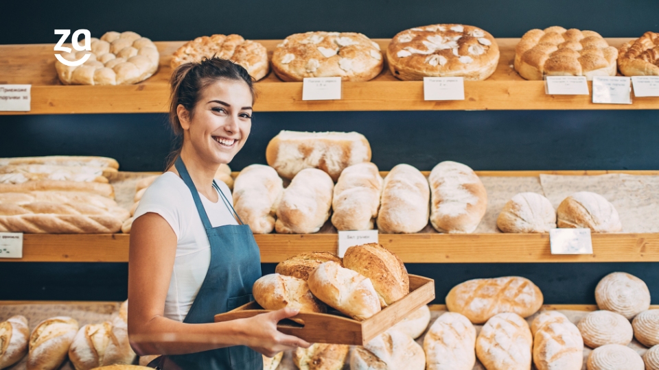 Dona e de padaria, a empreendedora segurando uma bandeja de pães caseiros.