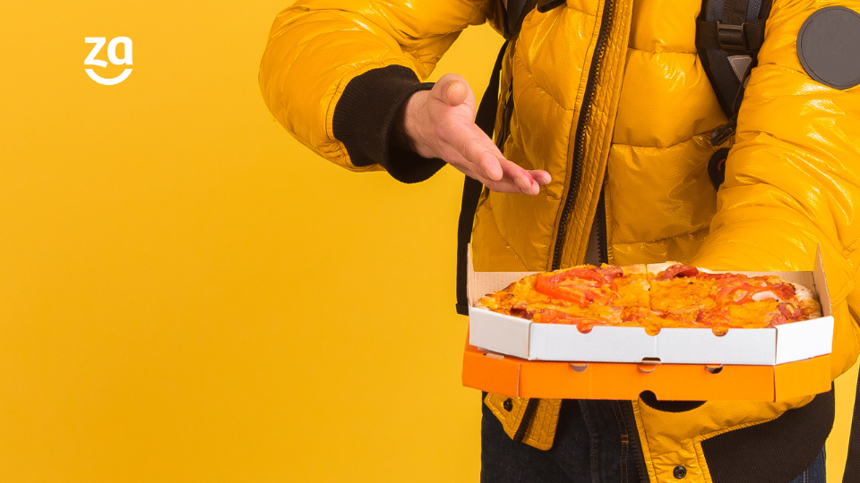 Entregador de delivery oferecendo pizza na foto, em fundo amarelo.