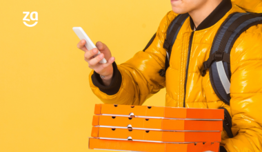 entregador delivery com pizzas, caixa de entrega e celular em fundo amarelo
