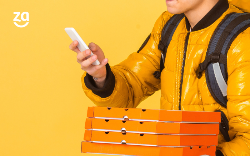 entregador delivery com pizzas, caixa de entrega e celular em fundo amarelo