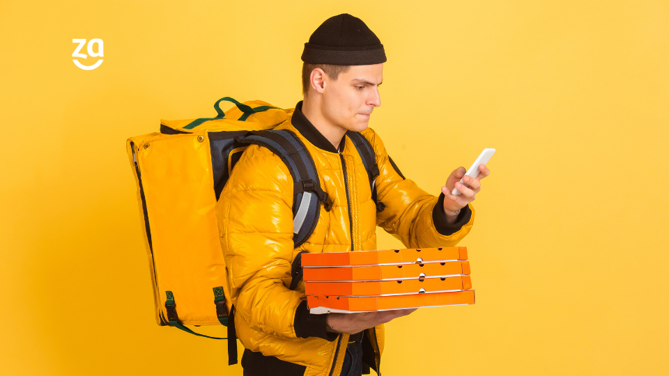 Homem com uniforme de entregador delivery segurando caixas de pizza e celular