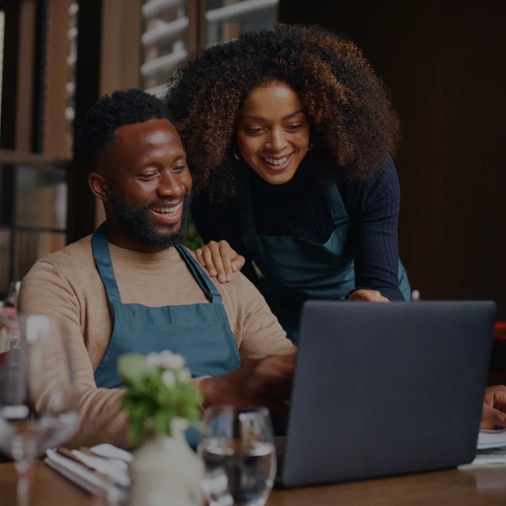 Um homem e uma mulher sorrindo enquanto olham para um computador.